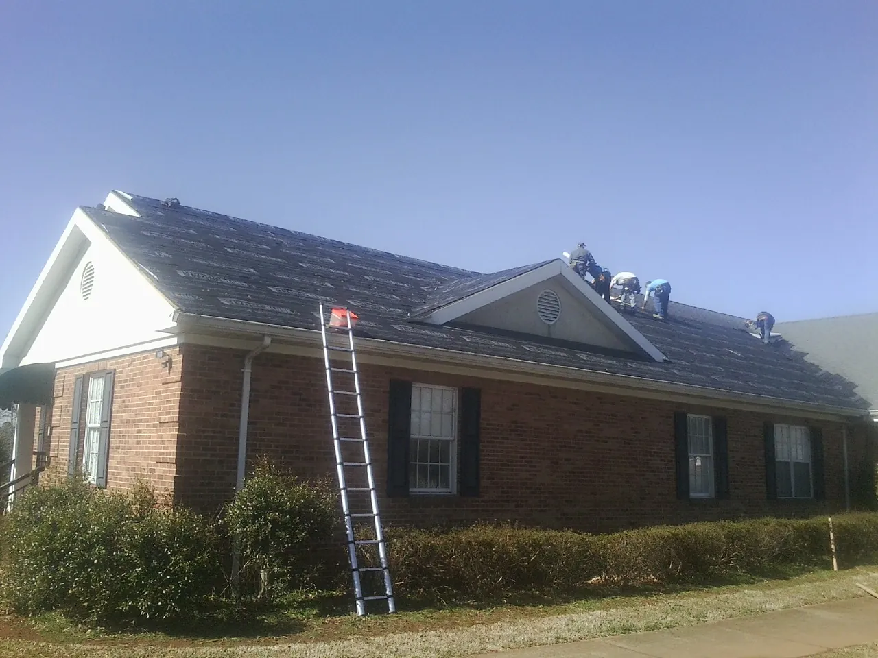 Crew tearing shingles off a brick ranch roof with a ladder set — Emergency Roof Repair work by our crew in Glencoe