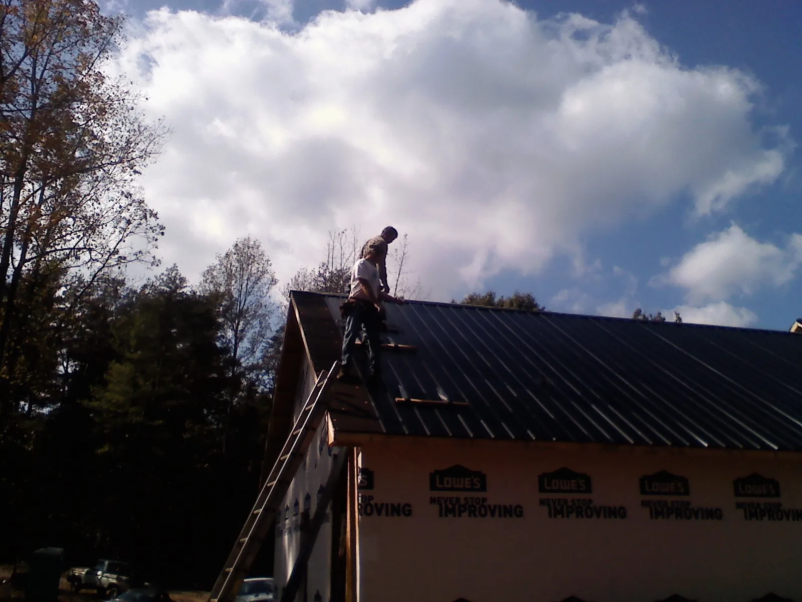 Roofer fastening dark metal panels high against a cloudy sky, from a Roof Inspection job in Glencoe